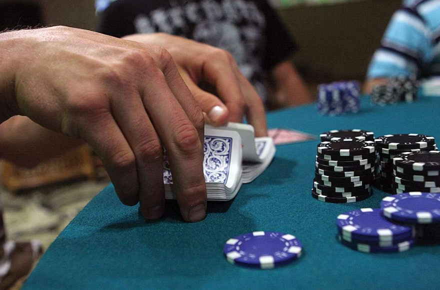 An intense poker game in a luxury casino showing a confident player making an aggressive bet with a large stack of chips while his opponent looks stressed.